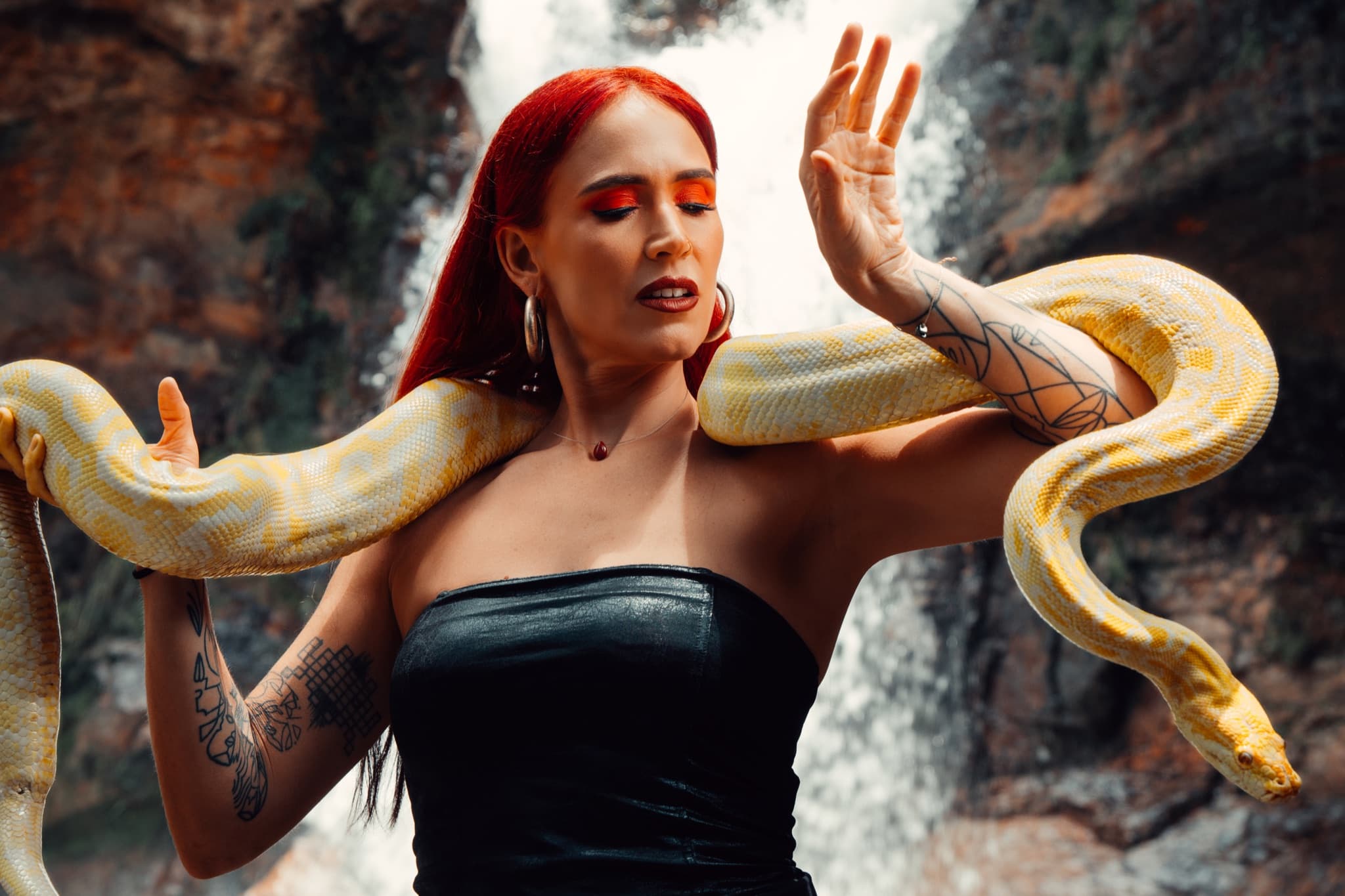 Retrato de moda con serpiente amarilla, vestuario negro y una cascada al fondo